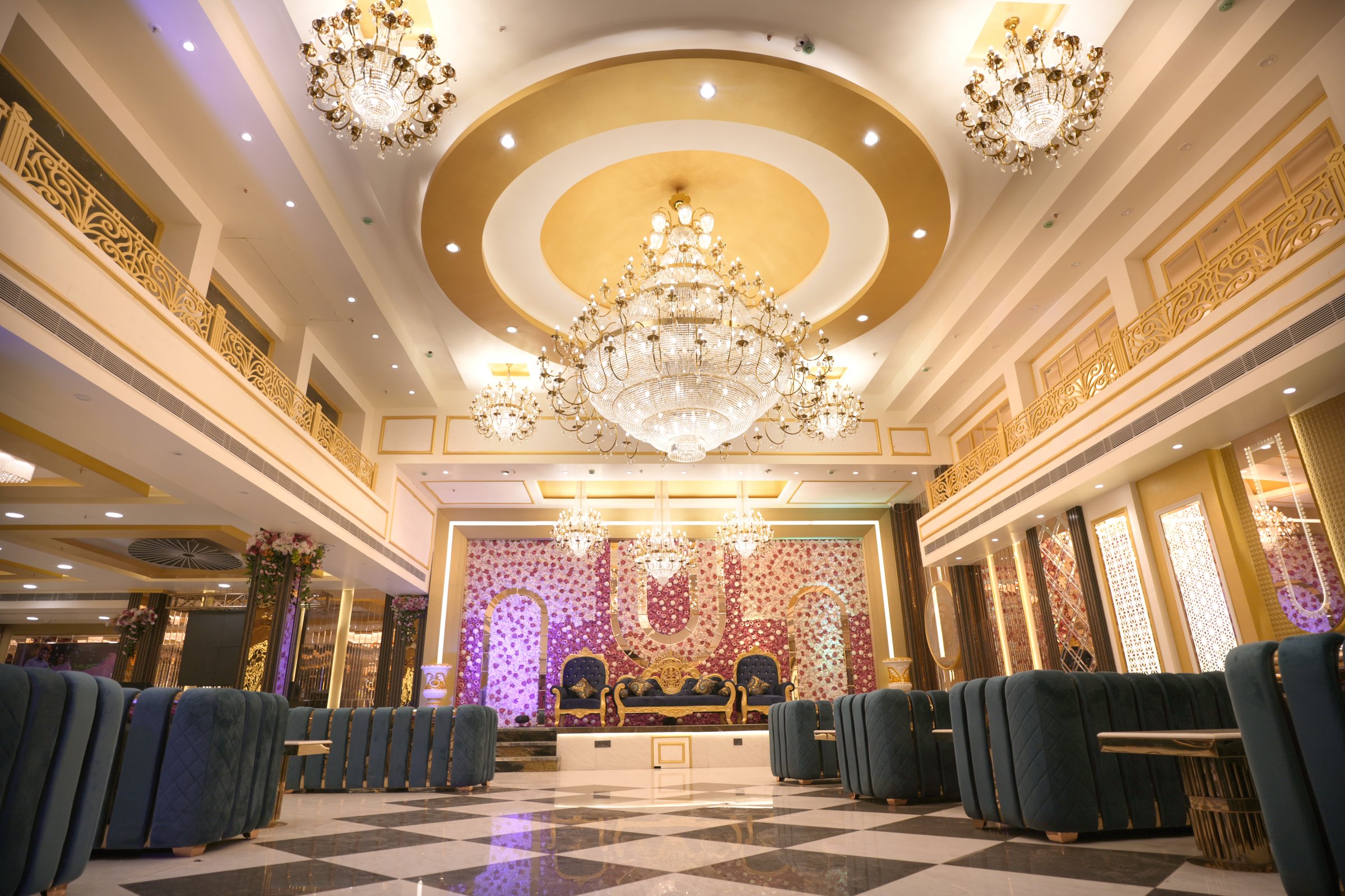 Grand banquet hall with massive crystal chandelier, floral wedding stage and gold luxury interiors at The Great Palace Banquet Hall, Seelampur