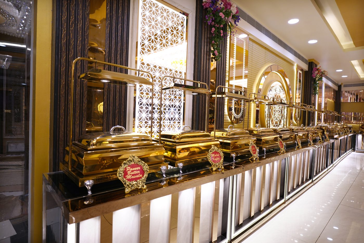 Luxury gold chafing dish buffet lineup with Paneer Butter Masala labels at The Great Palace Banquet Hall catering setup